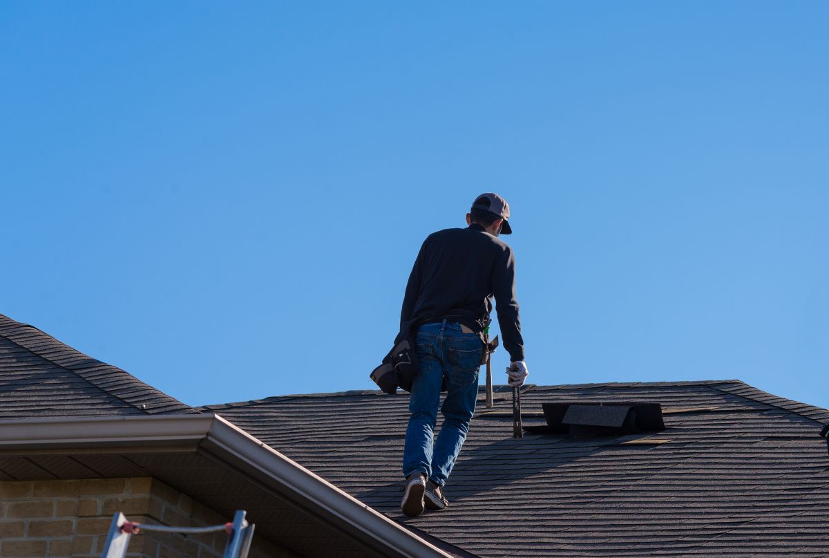 guy walking on top of shingles roof